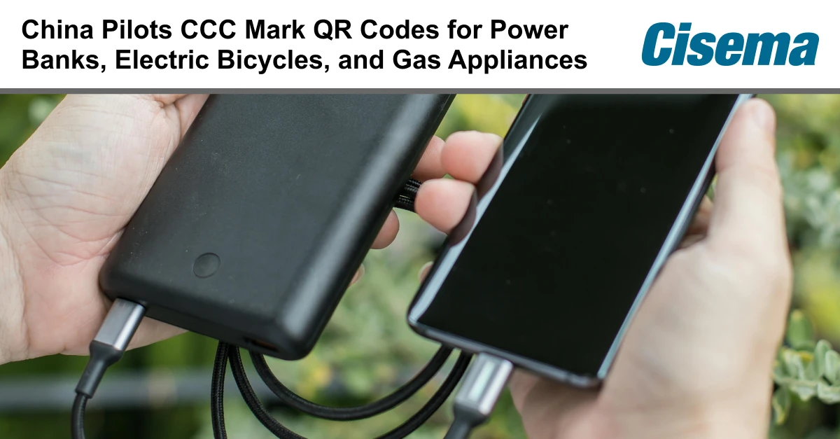 Banner image with headline text “China Pilots CCC Mark QR Codes for Power Banks, Electric Bicycles, and Gas Appliances” alongside the Cisema logo. Below, a close-up shows hands holding a black power bank connected by cables to a smartphone, illustrating device charging. The visual supports themes of product compliance, CCC certification, QR code traceability, and regulatory requirements for electronics and appliances in China and the Asia-Pacific market, relevant to market access and product registration.